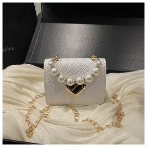 Detail of white woven straw bag with pearl handle, heart buckle and gold chain strap