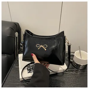 Close-up of black patent leather handbag with a gold bow detail on a stylish desk