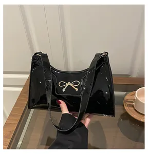 Detail of black patent leather baguette bag with golden bow hardware and shoulder strap