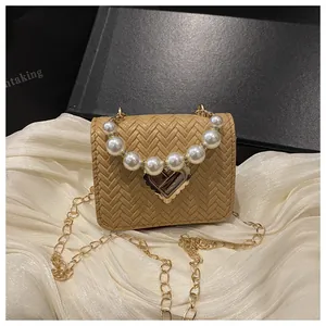 Detail of beige woven straw bag featuring pearl handle and gold heart clasp on silk