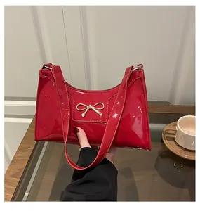 Detail of red patent leather baguette bag featuring a gold bow buckle on the front