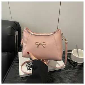Detail of pink crossbody bag featuring a delicate golden metal bow and fine PU leather texture