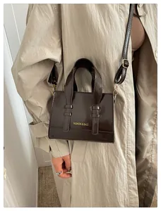 Detail of dark brown patent leather mini bag worn with a beige trench coat
