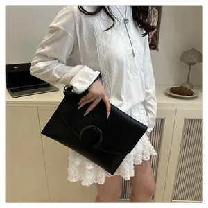 Detail of a large black leather envelope clutch with a metal horseshoe buckle in a lifestyle setting