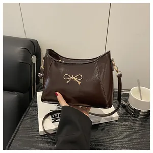 Detail of dark brown leather shoulder bag with elegant golden bow metal buckle accent