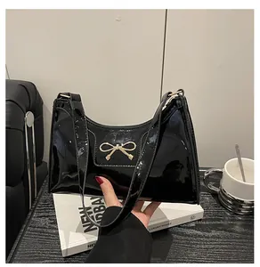 Detail of black patent leather hobo bag featuring a gold bow accent and zip closure