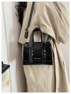 Detail of black leather handbag with gold hardware worn with a beige trench coat