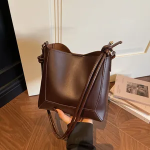 Deep brown matte leather bucket tote bag with knotted strap and folded base detail