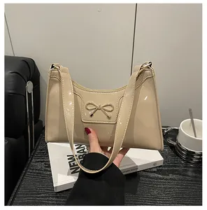 Detail of cream glossy patent leather baguette bag with golden metal bow buckle