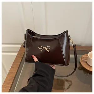 Close-up of a glossy dark brown shoulder bag featuring a gold metal bow and thin strap