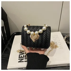 Detail of woven texture, pearl handle, and golden heart-shaped clasp on a mini crossbody bag