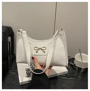 Close-up of white patent leather baguette bag featuring a gold bow hardware detail