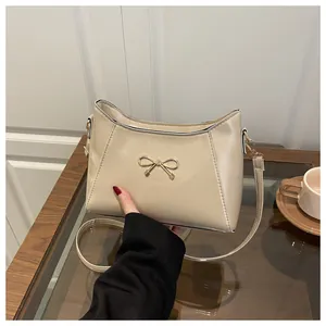 Detail of light beige shoulder bag featuring a gold metal bow and smooth PU leather