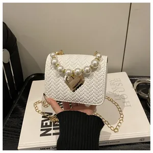 Detail of white woven crossbody bag featuring pearl handle and gold heart buckle