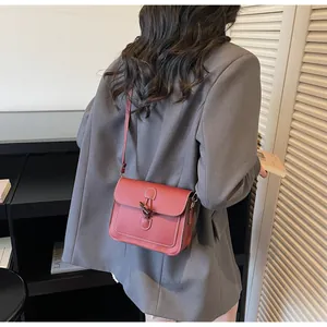 Detail of red vintage crossbody bag with horn buckle and contrast stitching on grey blazer