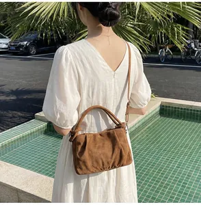 Outdoor shot showing a brown faux suede handbag with a pleated cloud design and shoulder strap