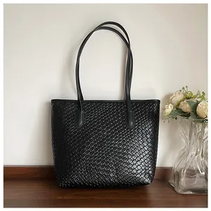 Detail shot of black woven texture leather tote bag on wooden table with elegant decor