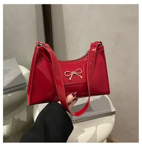 Close-up of a glossy red patent leather baguette bag with a gold metal bow buckle