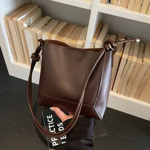 Detailed close-up of dark brown leather bucket bag with slim shoulder strap and knot detail