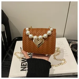 Detail of woven brown mini bag with pearl handle, heart lock, and gold chain strap