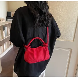 Detail of red faux suede handbag with soft pleats and sleek top handle on model