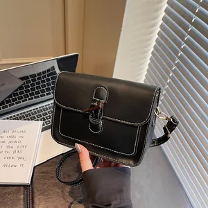 Close-up of black leather crossbody bag with white contrast stitching and wood toggle