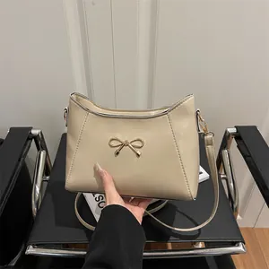Elegant off-white shoulder bag with gold bow decoration and sleek faux leather finish