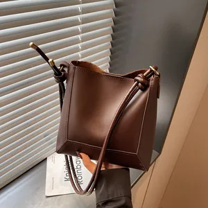 Detail of dark brown leather bucket bag with knotted shoulder strap and gold hardware
