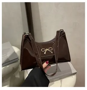 Close-up of dark brown patent leather baguette bag featuring a gold metal bow detail