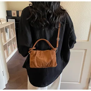 Brown faux suede crossbody bag with cloud pleats and top handle worn by a model