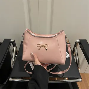 Pink faux leather shoulder bag with gold bow accessory shown from a front angle