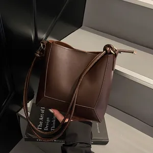 Detail view of deep brown leather bucket bag with knotted straps and geometric base