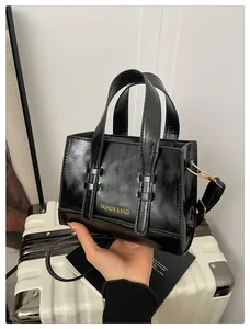Detail of black glossy leather tote bag with gold lettering and adjustable shoulder strap