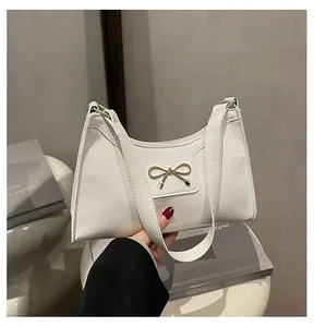 Close-up of white patent leather shoulder bag featuring a gold bow buckle detail
