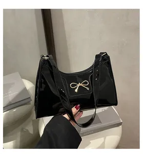 Close-up of black patent leather baguette bag featuring a gold bow-shaped metal buckle