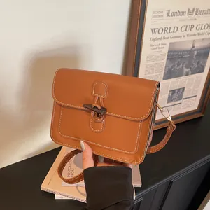 Detail of caramel brown square crossbody bag with contrast stitching and horn buckle closure
