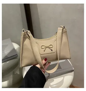 Detail of cream patent leather baguette bag with a gold metal bow clasp on a handle