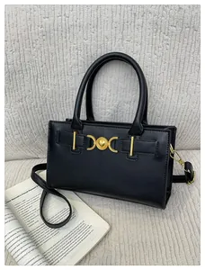 Detail of a black box handbag with golden heart clasp on a white textured sofa