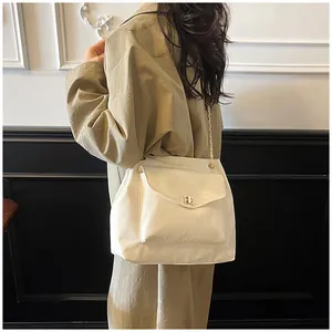 Détail du sac beige avec fermoir rotatif doré et bandoulière en chaîne métallique