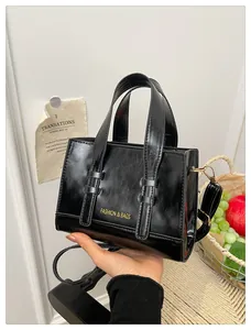 Close-up of black glossy PU leather handbag with gold buckle and fashion text detail