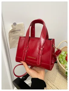 Detail of dark red glossy leather handbag featuring golden lettering and metal hardware