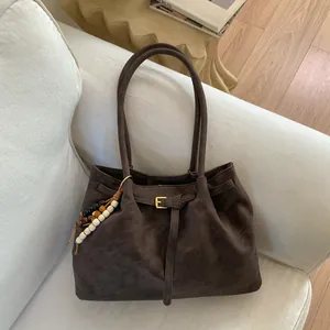 Borsa tote marrone scamosciata con ciondolo in legno su un divano bianco elegante