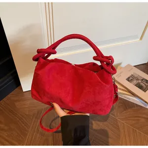 Close-up of red suede handbag featuring soft pleated silhouette and knotted handle detail
