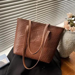 Brown woven texture tote bag with leather straps resting on a blazer in soft lighting