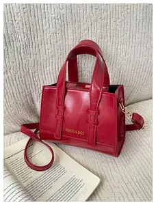 Detail of red glossy patent leather handbag with gold fashion lettering on white fabric