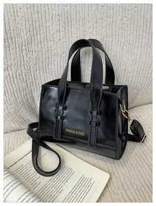 Detailed macro view of black glossy leather handbag with gold logo and shoulder strap