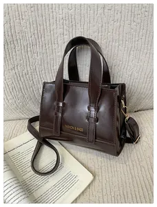Detail of a dark brown glossy leather handbag with gold buckles and fashion text