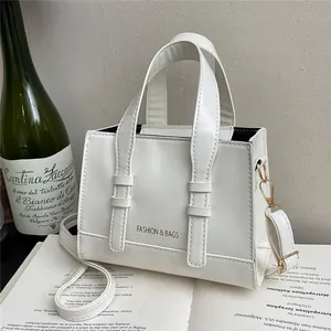 White vintage square handbag with top handles and adjustable strap on an open book