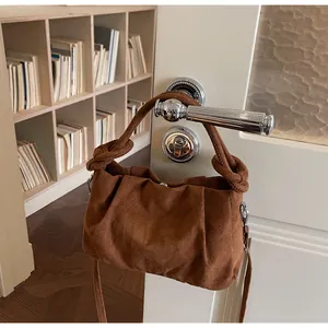 Detail of caramel suede-like crossbody bag with knotted handle on a white door