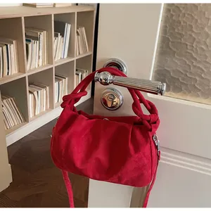Detail of red faux suede handbag with decorative knot hanging on a white wooden door